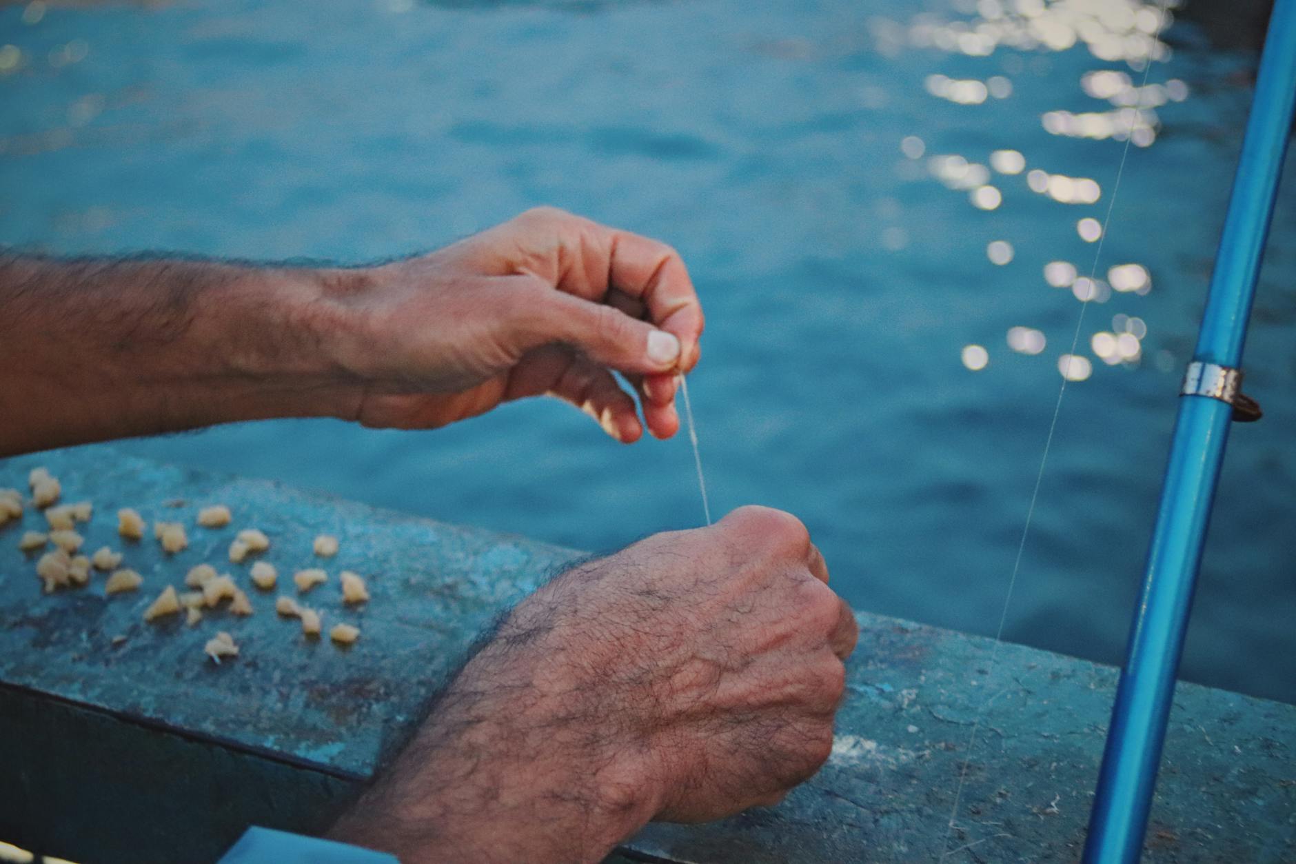 Dłonie nad wodą zakładają chleb na haczyk wędkarski