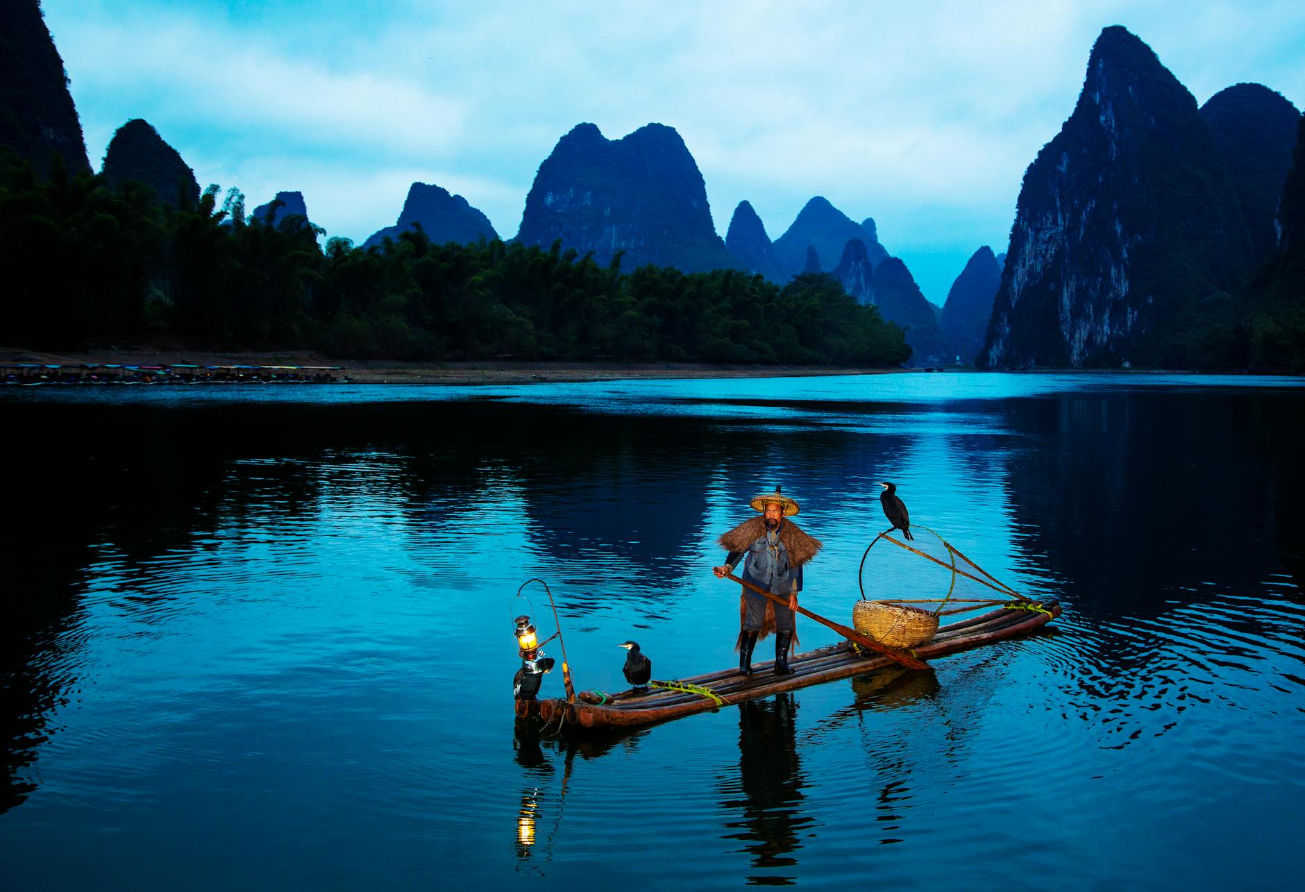 Rybak z kormoranem na rzece o zmierzchu wśród górskich wzgórz