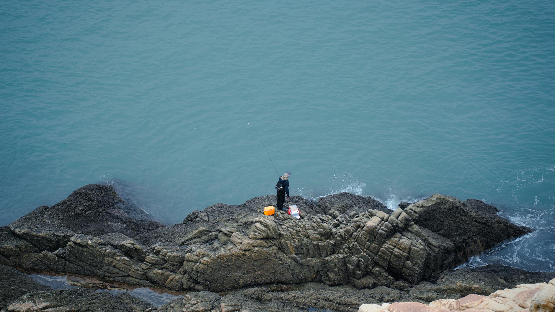 Wędkarz morski stoi na skałach nad Bałtykiem z wędką