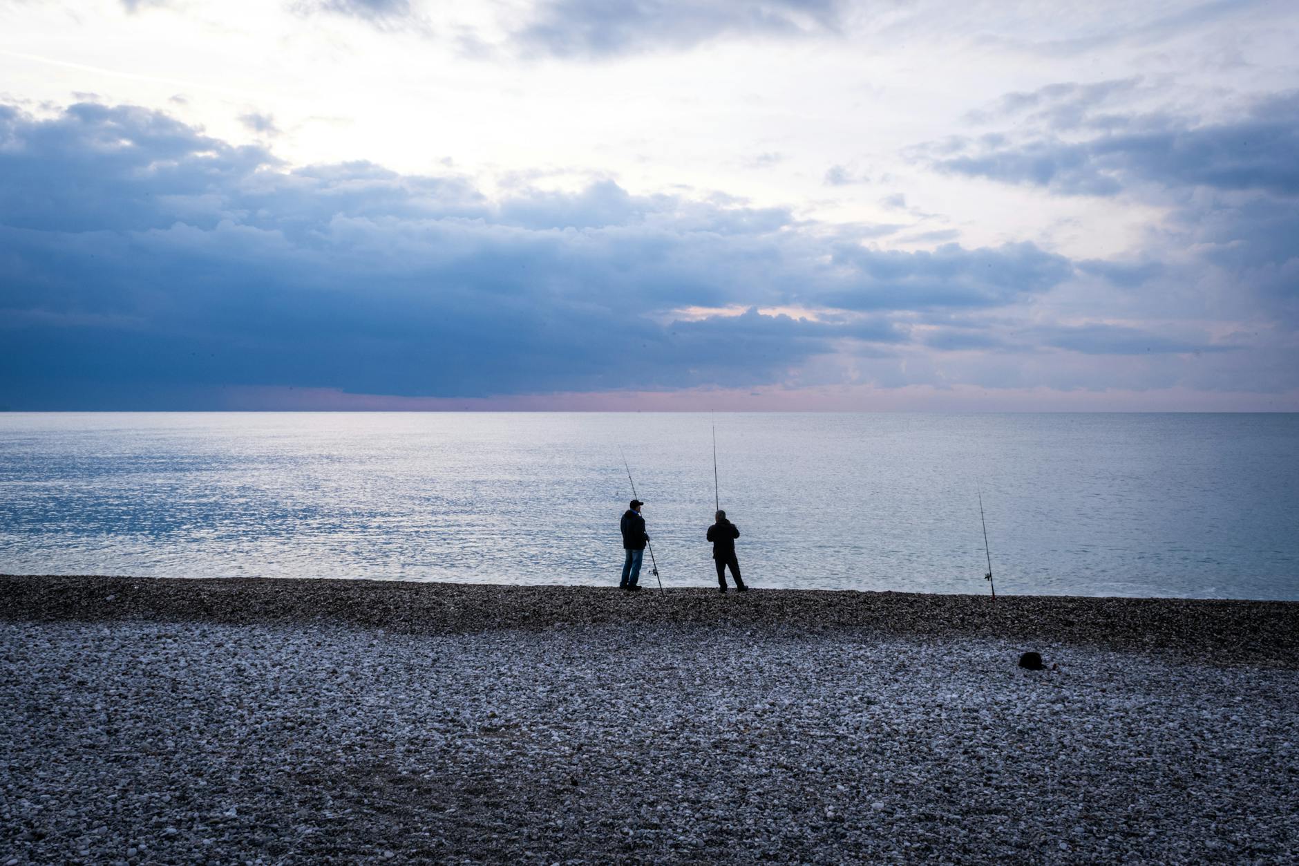 Wędkarze łowią z kamienistego brzegu Bałtyku o zmierzchu