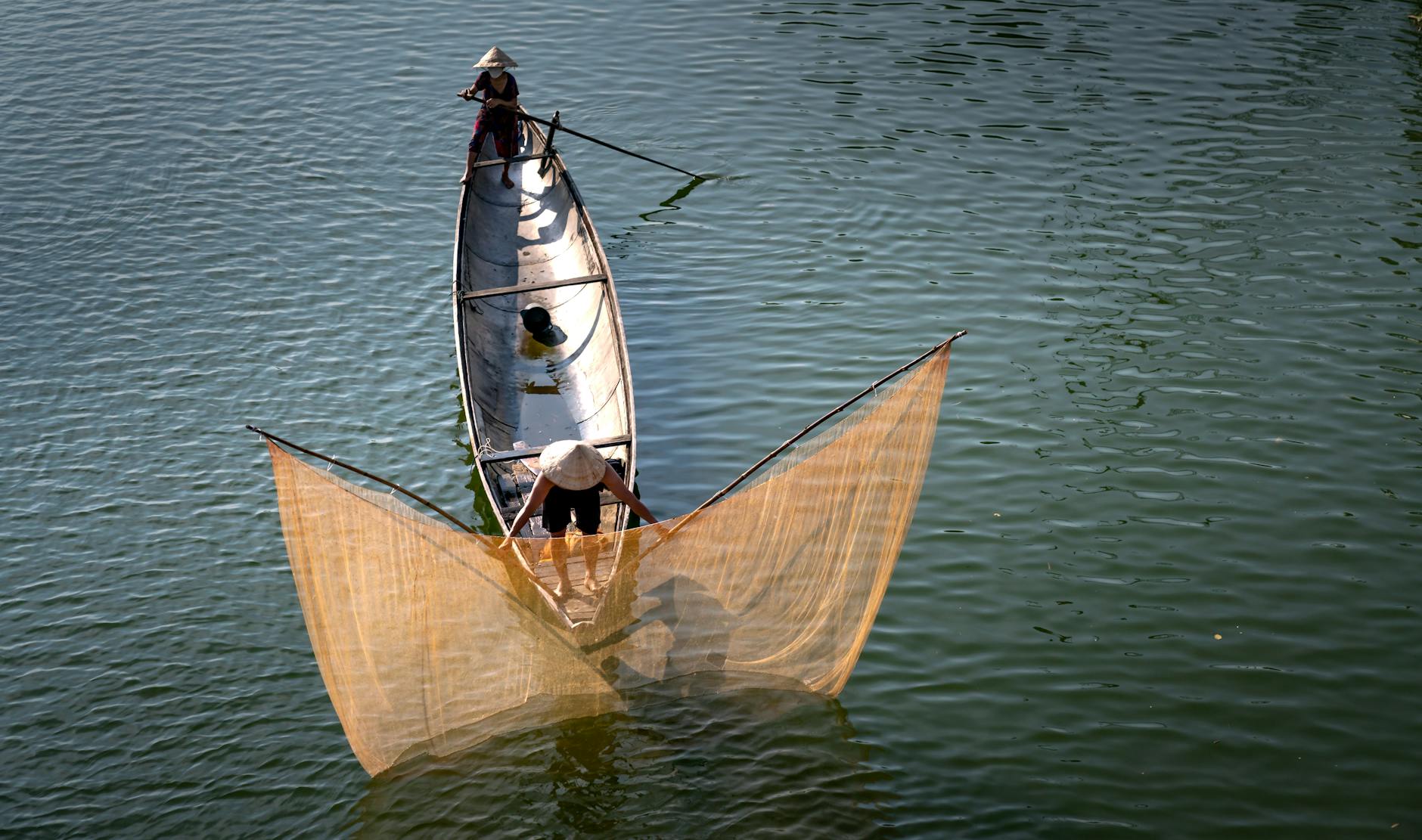 Wędkarze na łodzi zarzucają sieci na spokojnej rzece o zmierzchu