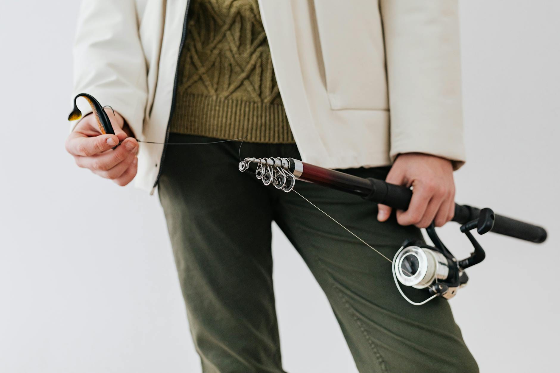 Osoba w odzieży outdoor trzyma wędkę z przynętą, zbliżenie na sprzęt