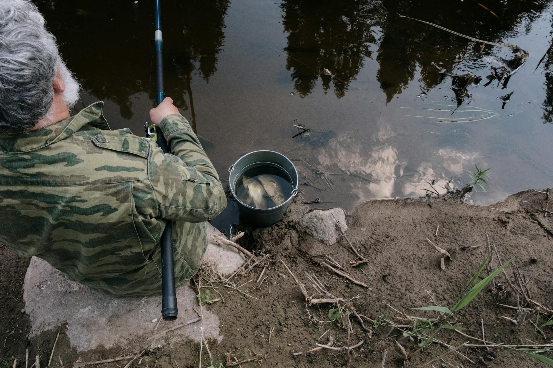 Starszy wędkarz ze spinningiem nad spokojną rzeką