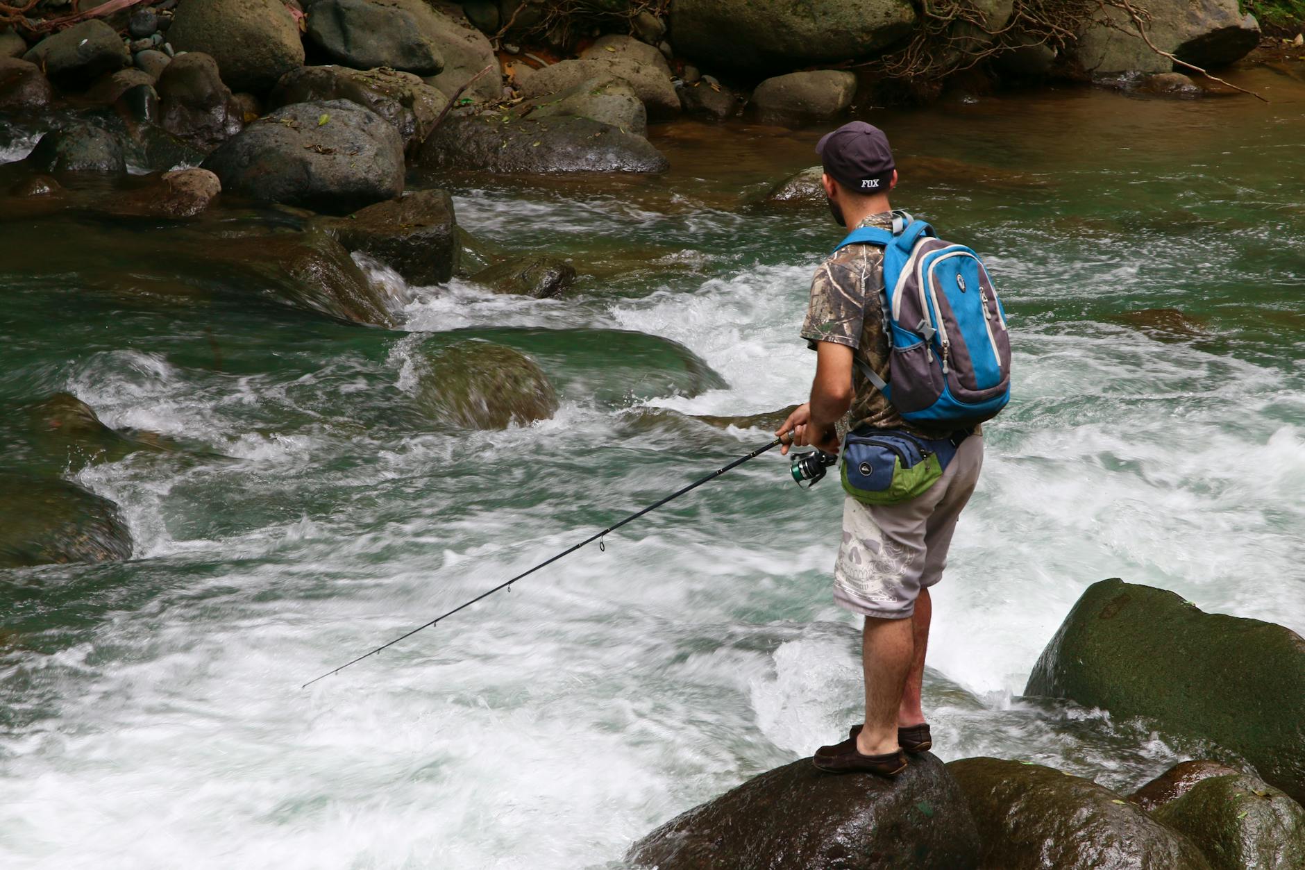 Wędkarz spinningowy z plecakiem łowi w kamienistym, płynącym potoku